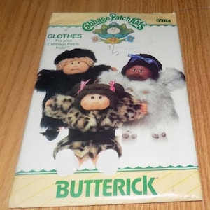 May include: A vintage Cabbage Patch Kids sewing pattern for making clothes for dolls. The pattern is for a leopard print coat, a white fur coat, and a black coat. The pattern number is 6984 and the brand is Butterick.