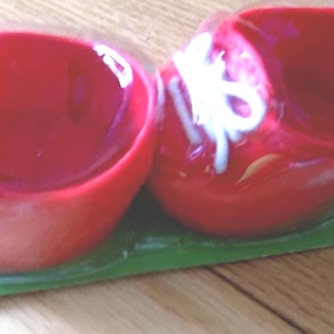 Könnte beinhalten: Zwei rote, herzförmige Behälter mit weißen Akzenten, möglicherweise zur Aufbewahrung kleiner Gegenstände oder als dekorative Elemente. Sie sind auf einer grünen Basis verpackt, was auf ein Einzelhandelsprodukt hindeutet.