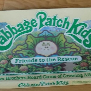 May include: A board game box for Cabbage Patch Kids, featuring a green and white illustration of a Cabbage Patch Kid with the text "Friends to the Rescue" and "Parker Brothers Board Game of Growing Affection".