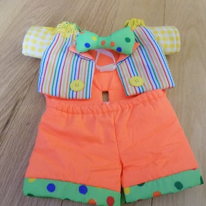 May include: A colorful clown costume for a stuffed animal, featuring a striped vest with yellow buttons, a green bow tie with white polka dots, and orange shorts with green, blue, and red polka dots.