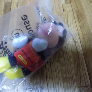 May include: A red, black, and yellow Mickey Mouse mini bean plush toy in a clear plastic bag with the words "Disney's" and "Mouse" printed on the bag.