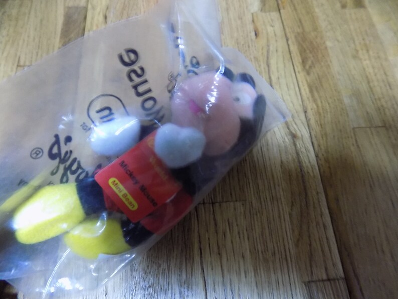 May include: A red, black, and yellow Mickey Mouse mini bean plush toy in a clear plastic bag with the words "Disney's" and "Mouse" printed on the bag.