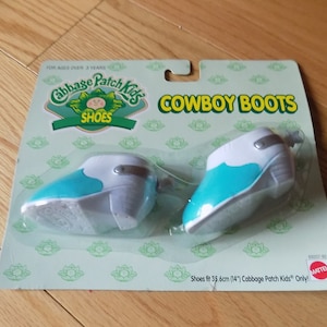 May include: A pair of blue and white cowboy boots for Cabbage Patch Kids dolls. The boots are packaged on a green and white card with the words "Cowboy Boots" and "Cabbage Patch Kids" printed on it. The card also includes the text "Shoes fit 35.6cm (14") Cabbage Patch Kids Only".