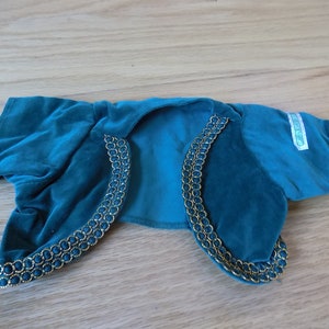 May include: Teal velvet jacket with gold trim. The jacket has short sleeves and a collar. The label reads "Care Bears".