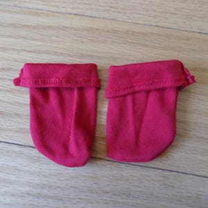 Könnte beinhalten: Zwei Paar rote Babysocken mit umgeschlagenen Bündchen. Die Socken sind aus einem weichen Material gefertigt und werden auf einer Holzoberfläche präsentiert. Die Socken haben eine einfarbige, leuchtend rote Farbe.