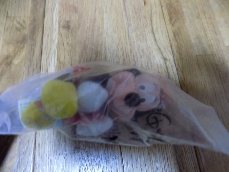 May include: A plush Mickey Mouse toy in a clear plastic bag. The toy is red, yellow, and white. The bag has a Disney logo on it.
