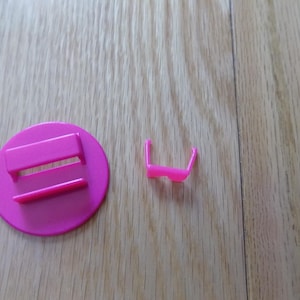 Puede incluir: Un conjunto de muebles de juguete de plástico rosa brillante. El conjunto incluye una base redonda con un banco y una silla pequeña. Las piezas son de plástico rosa vibrante.