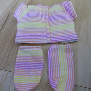 May include: A striped doll outfit with a pink, yellow, and orange color scheme. The outfit includes a short-sleeved shirt and two leg warmers.