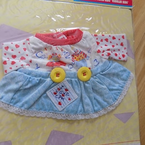 May include: A blue and white doll dress with a red and white heart print top. The dress has two yellow buttons and a white lace trim. The dress has a patch that says "I Love CPK".