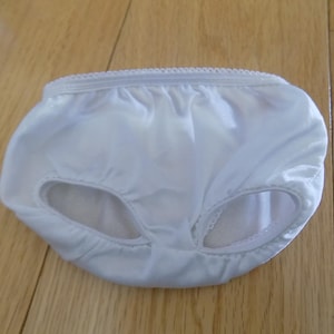 May include: White, silky underwear with elasticated leg openings and a decorative trim along the waistband. The garment is designed with a full coverage style. The fabric appears to be lightweight and slightly translucent.