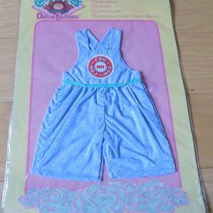 May include: A blue Cabbage Patch Kids Deluxe Fashions outfit with a white and blue pattern and a green belt. The outfit has a large Cabbage Patch Kids logo on the front.