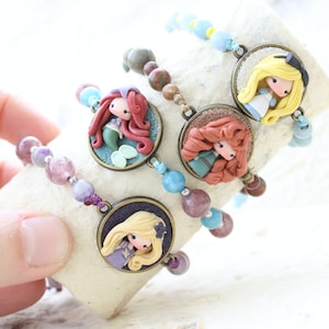 May include: Five colourful bracelets with round charms featuring different cartoon characters. Each charm has a different character with a unique hairstyle and outfit. The bracelets are made with various coloured beads and stones.