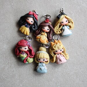 May include: A set of seven colourful princess-themed charms, each featuring a different Disney princess with a unique hairstyle and dress. The charms are made of polymer clay and have a silver loop for attaching to a necklace, bracelet, or keyring.