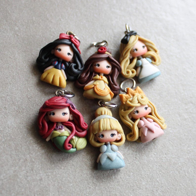 May include: Set of seven handmade polymer clay Disney princess charms. Each charm features a different princess in a colourful dress with detailed facial features and hair. The charms are perfect for adding a touch of Disney magic to your jewellery or crafts.