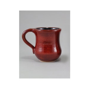 May include: A red ceramic mug with a rounded body and a black interior. The mug has a handle on the side.