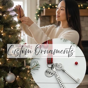 a woman hanging a custom new home ornament on a Christmas tree. Has an insert photo of a custom new home ornament with a long silver tag with the street address hand stamped, a circle tag with the current year the home was purchased, a silver skeleton key, and a tartan ribbon