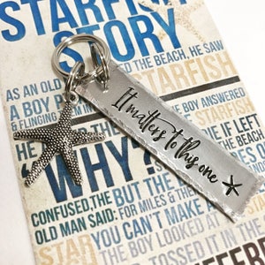 May include: A silver-toned metal keychain featuring a rectangular tag stamped with the text "It matters to this one" and a small starfish charm. The keychain is attached to a circular metal ring, resting against a card printed with text.