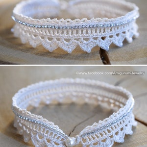 Puede incluir: Un collar gargantilla de crochet blanco con una fila de diamantes de imitaci&oacute;n y un acento de perla. El collar est&aacute; sobre una superficie de madera.