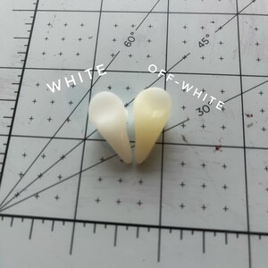 May include: Two heart-shaped pieces of white and off-white resin, labelled "WHITE" and "OFF-WHITE", on a white grid with markings for degrees and inches.