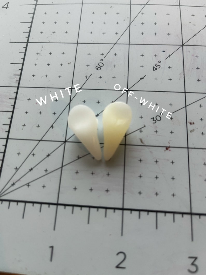 May include: Two heart-shaped pieces of white and off-white resin, labelled "WHITE" and "OFF-WHITE", on a white grid with markings for degrees and inches.