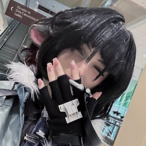 May include: A person with black hair and a white fur collar is wearing a gray jacket and black gloves. They are holding a white object in their hand and have their eyes closed.