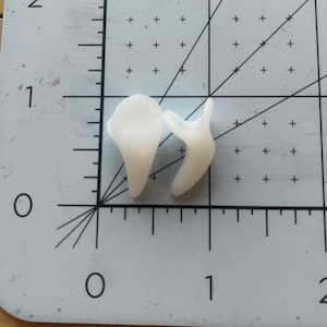 May include: Two white silicone earplugs, designed to block out noise. The earplugs are shown on a white grid background.