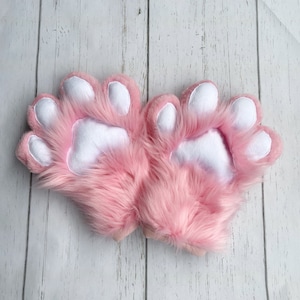 Op de afbeelding: Een paar roze, harige handpoppen in de vorm van poten met witte voetkussens.