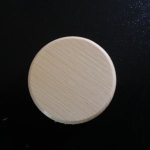 May include: A round, wooden disc with a light brown color and a smooth, slightly textured surface.