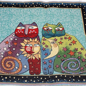 May include: A tapestry featuring two colorful cats with a sun and moon design. The cats are surrounded by stars and have a swirling pattern on their tails. The background is a light blue with a white polka dot pattern.