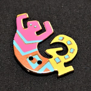 Puede incluir: Un botón de cerámica con un diseño de lagarto estilizado en rosa, amarillo y azul. El botón tiene dos agujeros para coser.