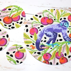 May include: Set of four round fabric coasters with a white background, black polka dots, and a colorful cherry and leaf design. A larger round fabric coaster with the same design features a purple monkey sitting on a branch.