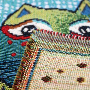 May include: Close-up of a colorful woven tapestry featuring a cartoon owl with large eyes. The owl is partially obscured by a second piece of tapestry with a geometric pattern.