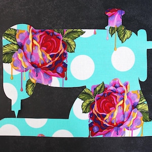Może przedstawiać: Wycięcie z tkaniny w kształcie maszyny do szycia. Maszyna jest jasnoniebieska z białymi kropkami i posiada dwie duże róże z czerwonymi, fioletowymi i żółtymi akcentami. Zielone liście i detale spływającej farby dopełniają projekt.