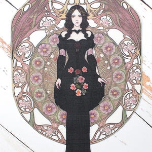 May include: An Art Nouveau style image of a woman in a black dress with floral accents. She is set against a circular backdrop with pink, green, and brown floral and geometric patterns. The design evokes a vintage aesthetic.