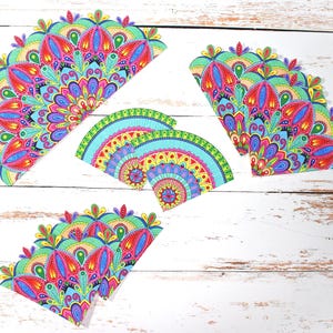 May include: Colorful, semi-circular mandala designs in shades of red, blue, green, and yellow. The intricate patterns are arranged on a white wooden surface. The designs are likely for crafts or decorative purposes.