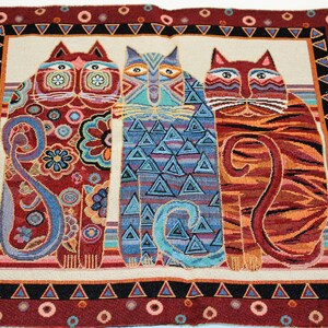 May include: A tapestry featuring three colorful cats with intricate patterns. The cats are standing side-by-side against a white background with a red, black, and white border.