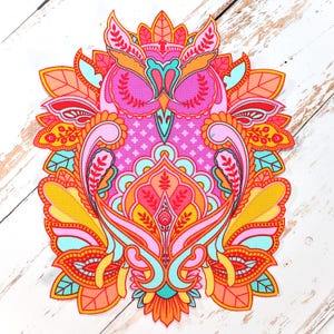 May include: A colorful, patterned owl design in shades of pink, orange, yellow, and teal. The owl features intricate floral and paisley details, with a symmetrical arrangement. The design is set against a white wooden background.
