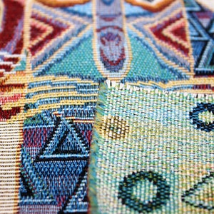 May include: Close-up of a colorful woven fabric with geometric patterns in shades of blue, red, green, and yellow. The fabric has a textured surface and a slightly frayed edge.