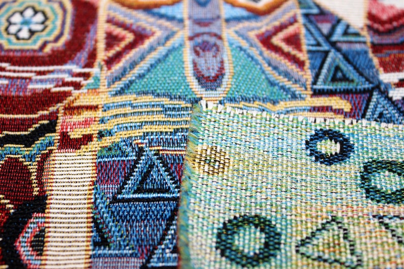 May include: Close-up of a colorful woven fabric with geometric patterns in shades of blue, red, green, and yellow. The fabric has a textured surface and a slightly frayed edge.