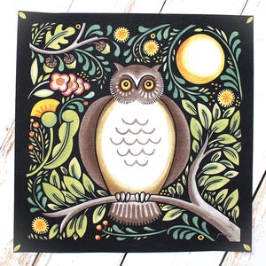 Op de afbeelding: Vierkante print met een bruine uil op een tak, omringd door groene bladeren, gele bloemen en een volle maan tegen een zwarte achtergrond. De uil heeft grote, gele ogen en een witte borst. Het kunstwerk is in folk art stijl.