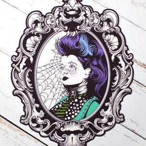 Może przedstawiać: Ornamentowane czarne i białe ramki z kobietą w środku, z fioletowymi i niebieskimi włosami. Kobieta ma za sobą pajęczynę i nosi zielono-czarną sukienkę w wzory.