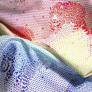 Peut inclure: Un tissu blanc orné d'un dégradé arc-en-ciel de pois et de petites formes d'étoiles, de lunes et de cœurs. Le motif présente des silhouettes de léopards répétées dans diverses couleurs, passant du bleu au jaune puis au rouge.