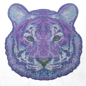 May include: A purple and blue tiger face design. The tiger's face is made up of small dots, with green eyes and white accents. The design is on a white background. The tiger's face is a unique and eye-catching piece of art.