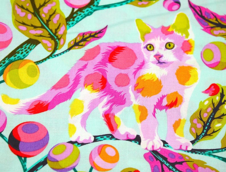 K&ouml;nnte beinhalten: Ein farbenfroher Stoff mit einer rosa Katze mit orangefarbenen und gelben Punkten auf hellblauem Hintergrund. Das Design umfasst stilisierte Bl&auml;tter und gemusterte Kugeln in verschiedenen Farben, wodurch ein skurriles, k&uuml;nstlerisches Muster entsteht.
