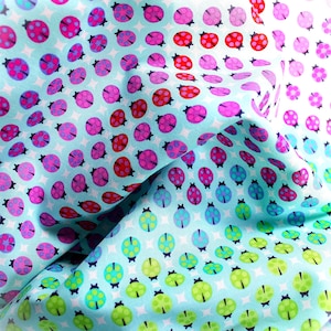 May include: A light blue fabric featuring a repeating pattern of ladybugs in various colors including red, pink, purple, blue, and green. The ladybugs are arranged in a grid-like formation against a background of small white four-pointed stars.