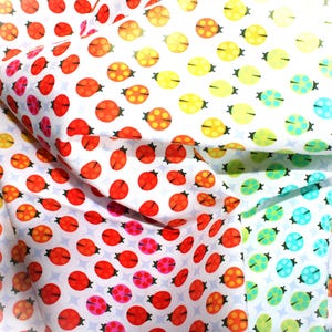 May include: A white fabric featuring a repeating pattern of ladybugs in a gradient of colors, transitioning from red and orange on the left to yellow, green, and light blue on the right, with a subtle star-shaped background texture.