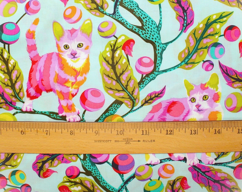 K&ouml;nnte beinhalten: Stoff mit einem skurrilen Design mit zwei stilisierten Katzen in rosa, orange und gelben Streifen und Flecken. Die Katzen sind vor einem hellblauen Hintergrund mit bunten, gemusterten Kugeln und Bl&auml;ttern platziert. Unten befindet sich ein Holzlineal.