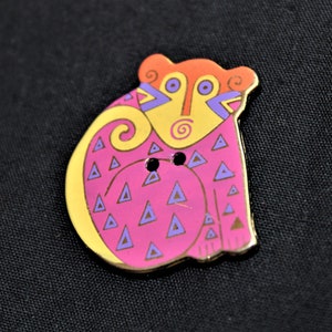 May include: A decorative button with a colorful design. The button features a stylized animal shape with a pink body, yellow accents, and purple triangles. The animal has an orange head and gold trim. Two small holes are visible.