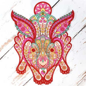 Könnte beinhalten: Ein farbenfrohes, gemustertes Dekorationsstück mit einem symmetrischen Design mit Blumen- und Blättermotiven. Der Artikel ist überwiegend rot, rosa, gelb und türkis, mit einer zentralen gesichtsähnlichen Form und flügelartigen Elementen.