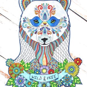 May include: A colorful illustration of a bear with intricate patterns and floral accents. The bear's face features blue, orange, and red designs, with the text "WILD & FREE" on a banner below. The artwork is set against a white wooden background.